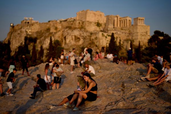 سائح يستخدم مروحة يدوية لتبريد نفسه خلال موجة حرّ، بينما يحتشد الناس على تلة آريوباغوس في اليونان، مع ظهور معبد الأكروبوليس في الخلفية. - سبوتنيك عربي