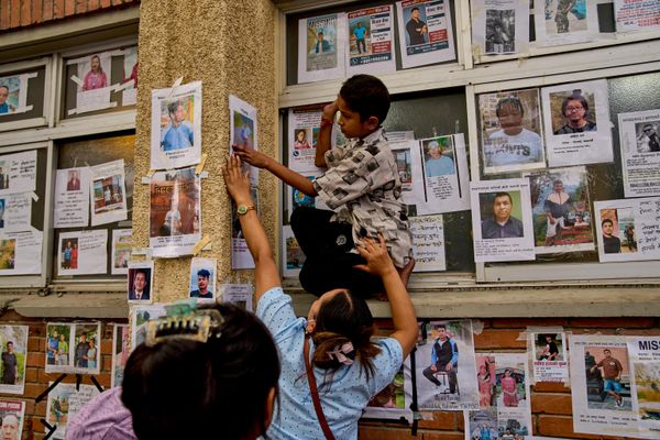 طفل صغير يساعد امرأة في تعليق صورة أحد أقاربها المفقودين على جدار بجانب صور لأشخاص مفقودين ومتوفين معروضة خارج مستشفى حكومي في كاتماندو - سبوتنيك عربي