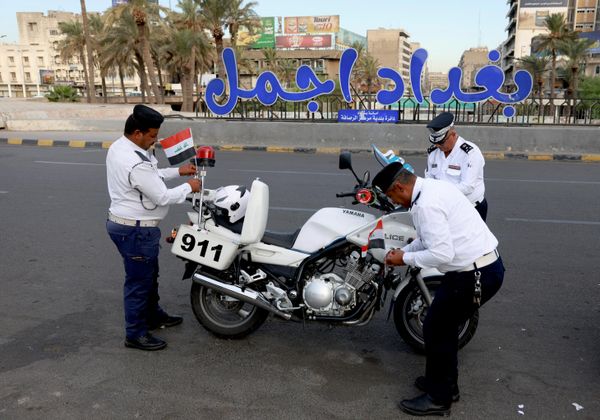 عناصر من شرطة المرور يزينون دراجة نارية تابعة للشرطة بالأعلام العراقية خلال "يوم السيادة"  الذي يتزامن مع انسحاب قوات "التحالف" - سبوتنيك عربي