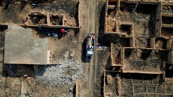 شاحنة تقل سكاناً عائدين مع ممتلكاتهم تمر بمحاذاة مبانٍ مدمرة في قرية العريشة بريف رأس العين في سوريا. - سبوتنيك عربي