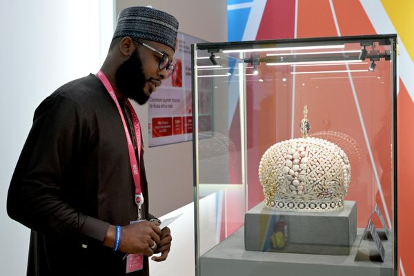 أحد زوار المعرض يقف أمام واجهة زجاجية تعرض مجسّمًا ذا تصميم هندسي، وتبرز في الخلفية لوحات تعريفية وديكورات بألوان الأحمر والأزرق والأبيض - سبوتنيك عربي