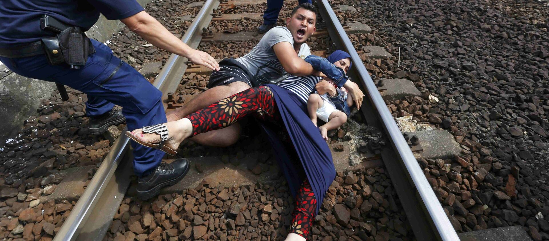 عناصر من الشرطة الهنغارية يحاولون منع أسرة من المهاجرين من العبور عبر محطة للسكك الحديدية المجر، 3 سبتمبر 2015. - سبوتنيك عربي, 1920, 18.07.2018