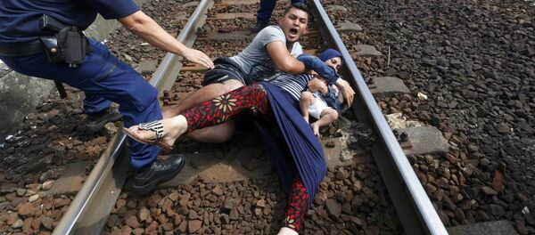 عناصر من الشرطة الهنغارية يحاولون منع أسرة من المهاجرين من العبور عبر محطة للسكك الحديدية المجر، 3 سبتمبر 2015. - سبوتنيك عربي