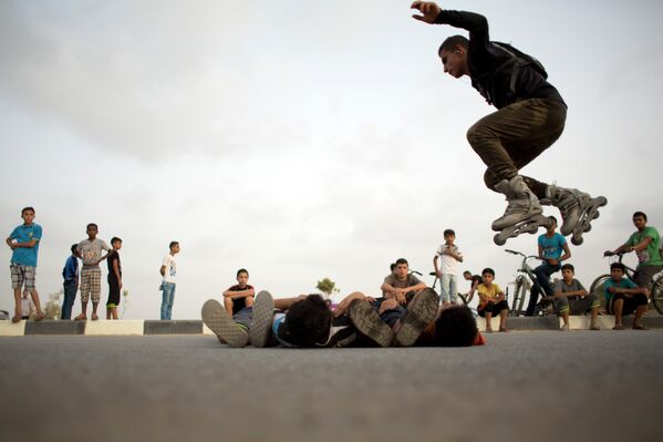 متزلج فلسطيني يقفز فوق الصبية الصغار نيام على الأرض ، وذلك خلال لقائهم الأسبوعي لممارسة رياضتهم في حي الزهراء، في ضواحي مدينة غزة. - سبوتنيك عربي