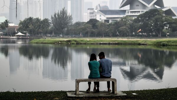 A Malaysian couple sit by a lake near the landmark Twin Towers (back R) on a hazy day in Kuala Lumpur - سبوتنيك عربي