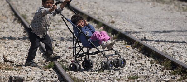 Мальчик везет коляску с ребенком в лагере беженцطفلين لاجئين، أحدهما يدفع بالآخر في قرية إيدوميني باليونان، 22 مايو/ آيار 2016.ев в Идомени, Греция - سبوتنيك عربي