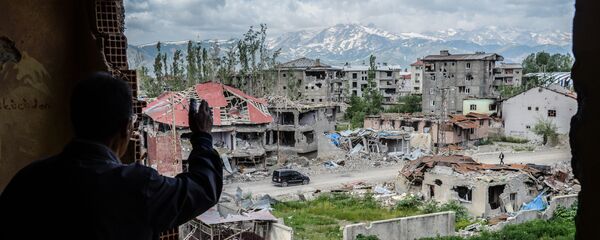 رجل يقف على خلفية ركام المباني في المنطقة التي تعرضت للاشتباكات بين القوات التركية والكردية في مدينة يوكسيكوفا بالقرب من الحدود مع العراق وإيران، 30 مايو/ آيار 2016. - سبوتنيك عربي