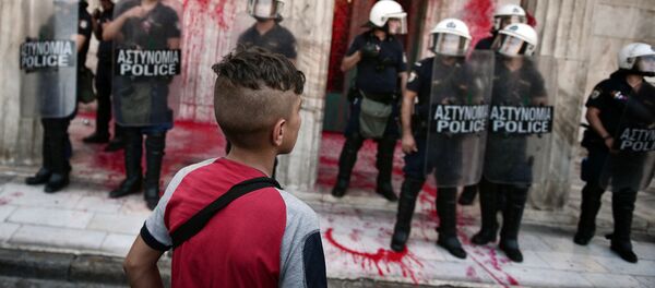 صبي ينظر إلى أفراد الشرطة الواقفين أمام مدخل لمبنى بلدية اليونان بعد أن قام مجموعات لمناصري المهاجرين واللاجئين بقذف طلاء أحمر على المبنى، 29 أغسطس/ آب 2016 - سبوتنيك عربي