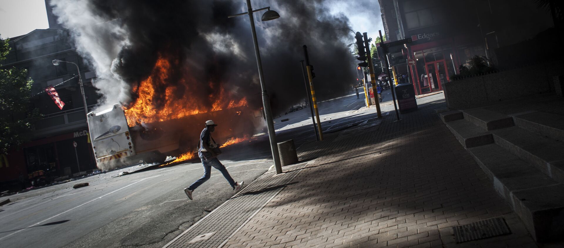أحد المتظاهرين يجري في الشارع بعد انفجار باص في جوهانسبرغ، جنوب أفريقيا 10 أكتوبر/ تشرين الأول 2016 - سبوتنيك عربي, 1920, 11.07.2021
