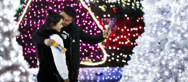 حبيبان، رجل وامرأة يلتقطان صورة سيلفي على خلفية أضواء أعياد رأس السنة في بكين، 1 ديسمبر/ كانون الأول 2016 - سبوتنيك عربي