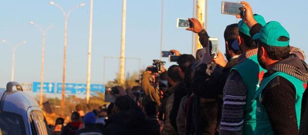 سوريون في حلب يشاهدون مغادرة الحافلات الخضراء التي تنقل المسلحين وأفراد أسرهم، 15 ديسمبر/ كانون الأول 2016 - سبوتنيك عربي