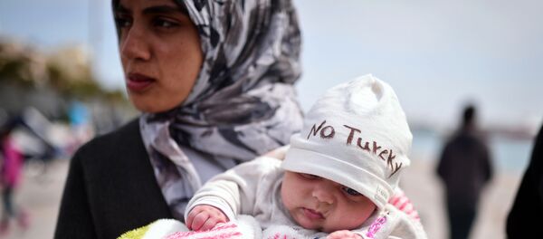 A Syrian refugee holds a two-month old baby as refugees and migrants who broke out from Chios detention camp, and camped out in the port of the city, stage a protest with their children chanting 'No Turkey' on April 3, 2016. - سبوتنيك عربي