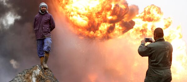 رجل يلتقط صورة لصديقه، بينما يقف الأخير على خلفية نيران مشتعلة ودخان كثيف، نتيجة اندلاع الحرائق في آبار نفط في القيارة، العراق، 30 يناير/ كانون الثاني 2017 - سبوتنيك عربي