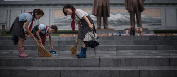 تلاميذ ينظفون الدرج الذي يقود إلى تماثيلي الزعيمين الكوريين الشماليين الراحلين كيم إيل سونغ وكيم جونغ إيل، على تلة مانسو حيث تصادف البلاد يوم النصر فى بيونغ يانغ، كوريا الشمالية فى 27 يوليو/ تموز 2017 - سبوتنيك عربي