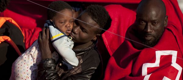 A migrants wrapped in a red cross blanket holds a child on arrival into the southern Spanish port of Malaga on January 27, 2016 after an inflatable boat carrying 55 Africans, seven of them women and six chidren, was rescued by the Spanish coast guard off the Spanish coast (File) - سبوتنيك عربي