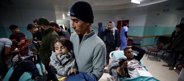 فلسطيني يحمل ابنته الجريحة وهي تنتظر تلقي العلاج بعد غارات جوية إسرائيلية قريبة من مستشفى في شمال قطاع غزة - سبوتنيك عربي