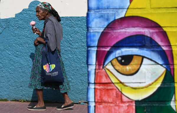 امرأة تسير حاملة مثلجات على خلفية جدارية في شارع فال دي أنجلوس، شمال تيغوسيغالبا في هندوراس 8 أبريل/ نيسان 2018 - سبوتنيك عربي