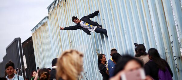 رجل يتسلق السياج الحدودي بين المكسيك والولايات المتحدة كجزء من المظاهرة، حيث يجتمع أعضاء من قافلة المهاجرين من أمريكا الوسطى قبل الاستعدادات لطلب اللجوء في الولايات المتحدة ، في تيخوانا، المكسيك 29 أبريل/ نيسان 2018 - سبوتنيك عربي