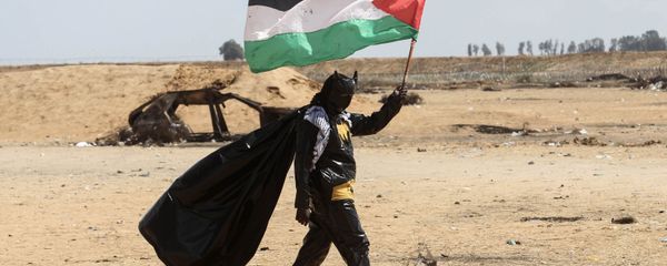 شاب فلسطيني يحمل العلم الفلسطيني، مرتديا زي ارجل الوطواط، خلال فعاليات مسيرات العودة في شرق خانيونس، على الحدود بين قطاع غزة وإسرائيل، 9 مايو/ أيار 2018 - سبوتنيك عربي
