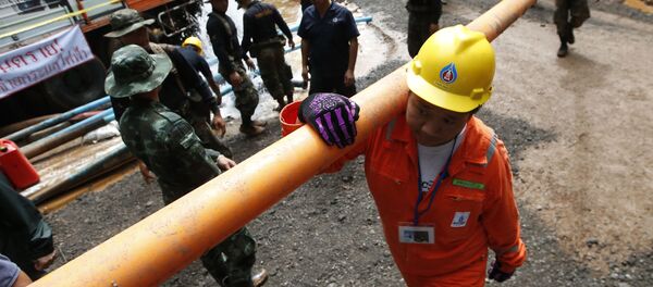 منقذ يحمل أنابيب المياه عند مدخل مجمع الكهوف حيث حوصر 12 صبيا ومدربي كرة القدم في الداخل عندما غمرت الأمطار الغزيرة الكهف في ماي ساي، محافظة تشيانج راي شمال تايلاند، 4 يوليو/ تموز 2018 - سبوتنيك عربي