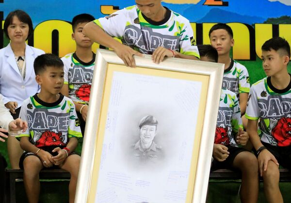 صبية كهف تايلاند يحملون في مؤتمر صحفي صورة مرسومة للغواص الذي لاقى حتفه أثناء محاولته إنقاذهم، 18 يوليو/تموز 2018 صبية كهف تايلاند يحملون في مؤتمر صحفي صورة مرسومة للغواص الذي لاقى حتفه أثناء محاولته إنقاذهم، 18 يوليو/تموز 2018 - سبوتنيك عربي