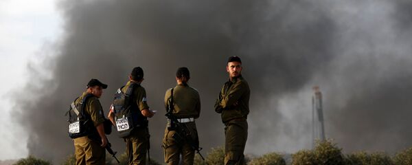 جنود إسرائيليون بالقرب من السياج الحدودي على الجانب الإسرائيلي من الحدود مع قطاع غزة واحتجاج فلسطينيين على الجانب الآخر - سبوتنيك عربي