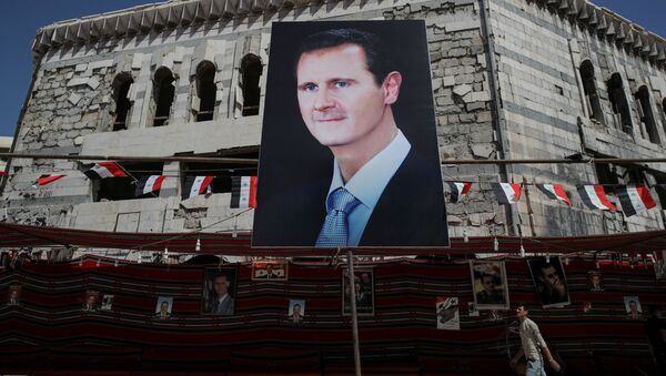 رجل يسير على خلفية لافتة تحمل صورة الرئيس السوري بشار الأسد في دوما، سوريا  17 سبتمبر/ أيلول 2018 - سبوتنيك عربي