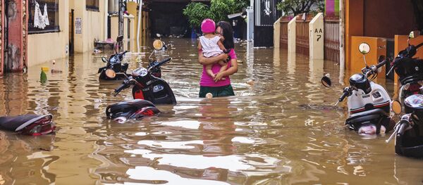 امرأة تحمل طفلها وسط مياه غمرت شوارع حي ماكاسار، إثر هطول أمطار غزيرة في إندونيسيا، 23 يناير/ كانون الثاني 2019 - سبوتنيك عربي