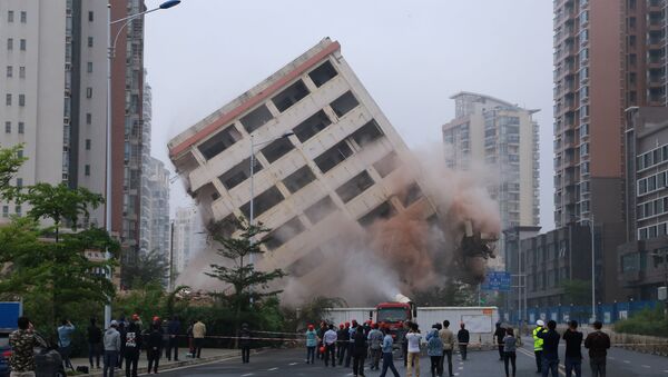 مواطنون يراقبون عملية هدم مبنى مكون من ثمانية طوابق يقع على طريق في هايكو بمقاطعة هاينان، الصين في 24 فبراير/ شباط 2019 - سبوتنيك عربي