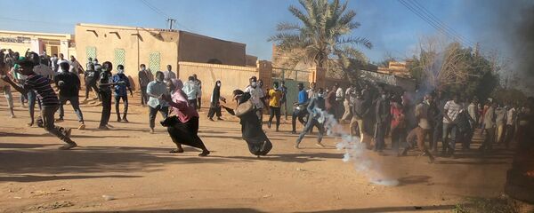 متظاهرون سودانيون يركضون من عبوة غاز مسيل للدموع أطلقها رجال شرطة مكافحة الشغب لتفريقهم وهم يشاركون في مظاهرات مناهضة للحكومة في أم درمان بالخرطوم - سبوتنيك عربي