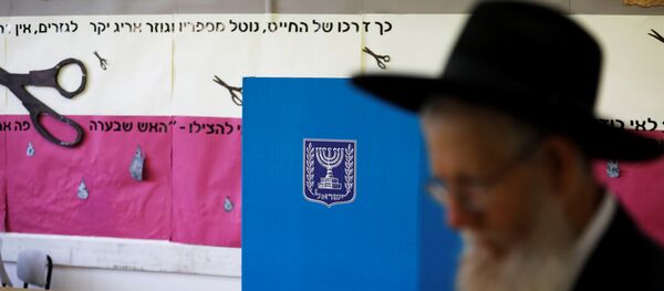 رجل يهودي متشدد يمشي بجانب كشك الاقتراع وصندوق الاقتراع في مركز اقتراع بينما يصوت الإسرائيليون في الانتخابات البرلمانية في القدس - سبوتنيك عربي