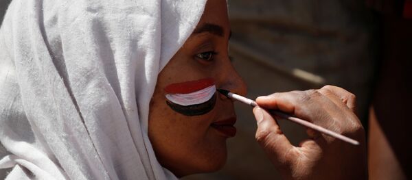 رجل يرسم العلم السوداني على وجه المتظاهرين في الخرطوم - سبوتنيك عربي