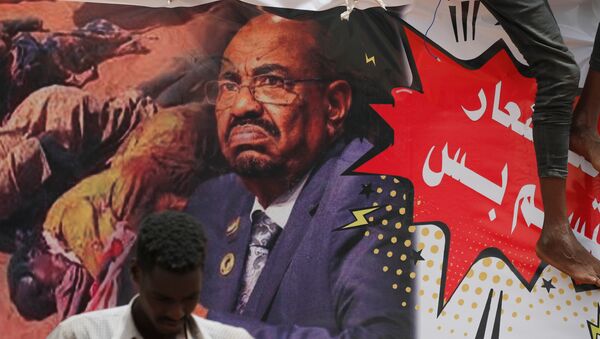 متظاهر يقف أمام لافتة تصور الرئيس السوداني السابق عمر البشير أمام وزارة الدفاع في الخرطوم - سبوتنيك عربي