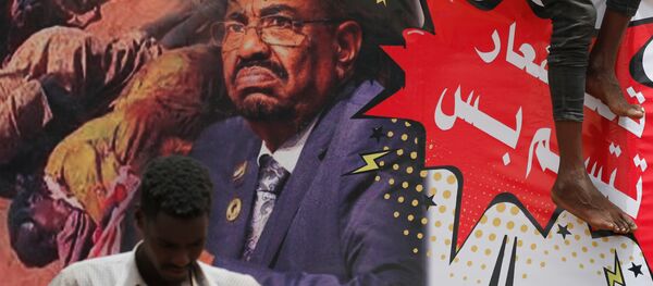 متظاهر يقف أمام لافتة تصور الرئيس السوداني السابق عمر البشير أمام وزارة الدفاع في الخرطوم - سبوتنيك عربي