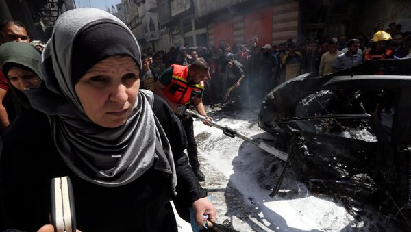 سيدة فلسطينية تمر في أثناء إخماد حريق في سيارة القيادي الحمساوي حامد أحمد عبد الخضري الذي قتل في غارة جوية إسرائيلية في مدينة غزة - سبوتنيك عربي
