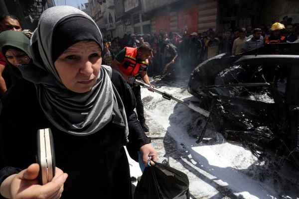 سيدة فلسطينية تمر في أثناء إخماد حريق في سيارة القيادي الحمساوي حامد أحمد عبد الخضري الذي قتل في غارة جوية إسرائيلية في مدينة غزة - سبوتنيك عربي