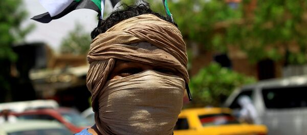 عضو في تحالف المعارضة والمجموعات الاحتجاجية في السودان يرتدي العلم الوطني وهو يهتف بشعارات خارج البنك المركزي السوداني - سبوتنيك عربي