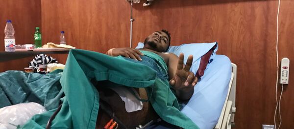 مصاب بعيار ناري في الحملة على المتظاهرين السودانيين يلوح بعلامة النصر داخل وهو يتلقى العلاج في مستشفى بالخرطوم - سبوتنيك عربي