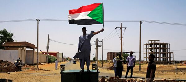 متظاهر سوداني يحمل راية وطنية وهو يقف على أحد المتاريس على طول شارع يطالب المجلس العسكري الانتقالي في البلاد بتسليم السلطة إلى المدنيين متظاهر سوداني يحمل راية وطنية وهو يقف على أحد المتاريس على طول شارع يطالب المجلس العسكري الانتقالي في البلاد بتسليم السلطة إلى المدنيين - سبوتنيك عربي