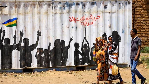 مدنيون يعبرون أمام كتابة على الجدران باللغة العربية الحرية والسلام والعدالة والمدنية في منطقة بري بالخرطوم - سبوتنيك عربي