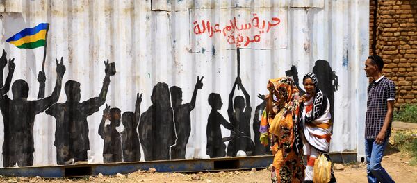مدنيون يعبرون أمام كتابة على الجدران باللغة العربية الحرية والسلام والعدالة والمدنية في منطقة بري بالخرطوم - سبوتنيك عربي