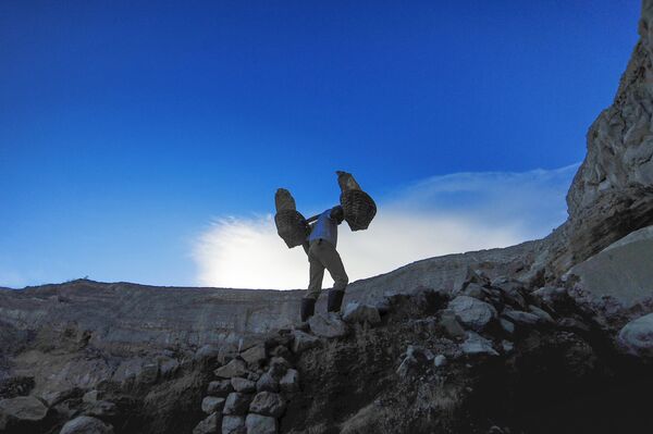 عامل منجم ينقل سلال الكبريت الصلب من مقلع يقع على البركان النشط كواه آيجن (Kawah Ijen) في إندونيسيا. يسود الفقر في المنطقة، والعمال ليس لديهم ملابس خاصة لهذه الوظيفة، ومتوسط الأجور، يتراوح بين 7-8 دولارات في اليوم. يقوم كل عامل منجم بنقل 75-90 كغم من الكبريت من المنجم في رحلة واحدة. - سبوتنيك عربي
