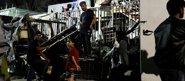 مهاجرون يقفون أمام حاويات محترقة في أعقاب نشوب حريق في مخيم موريا بجزيرة ليسبوس باليونان - سبوتنيك عربي