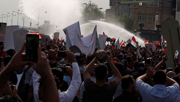 المتظاهرون يتفرقون بينما تستخدم قوات الأمن العراقية المياه خلال مظاهرة احتجاج على فساد الحكومة وسط استياء من قلة الوظائف والخدمات في ميدان التحرير في بغداد - سبوتنيك عربي