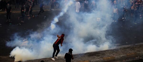  متظاهر يرمي علبة غاز مسيل للدموع تستخدمها قوات الأمن العراقية بينما يتفرق آخرون خلال مظاهرة احتجاج على البطالة والفساد وضعف الخدمات العامة في بغداد - سبوتنيك عربي