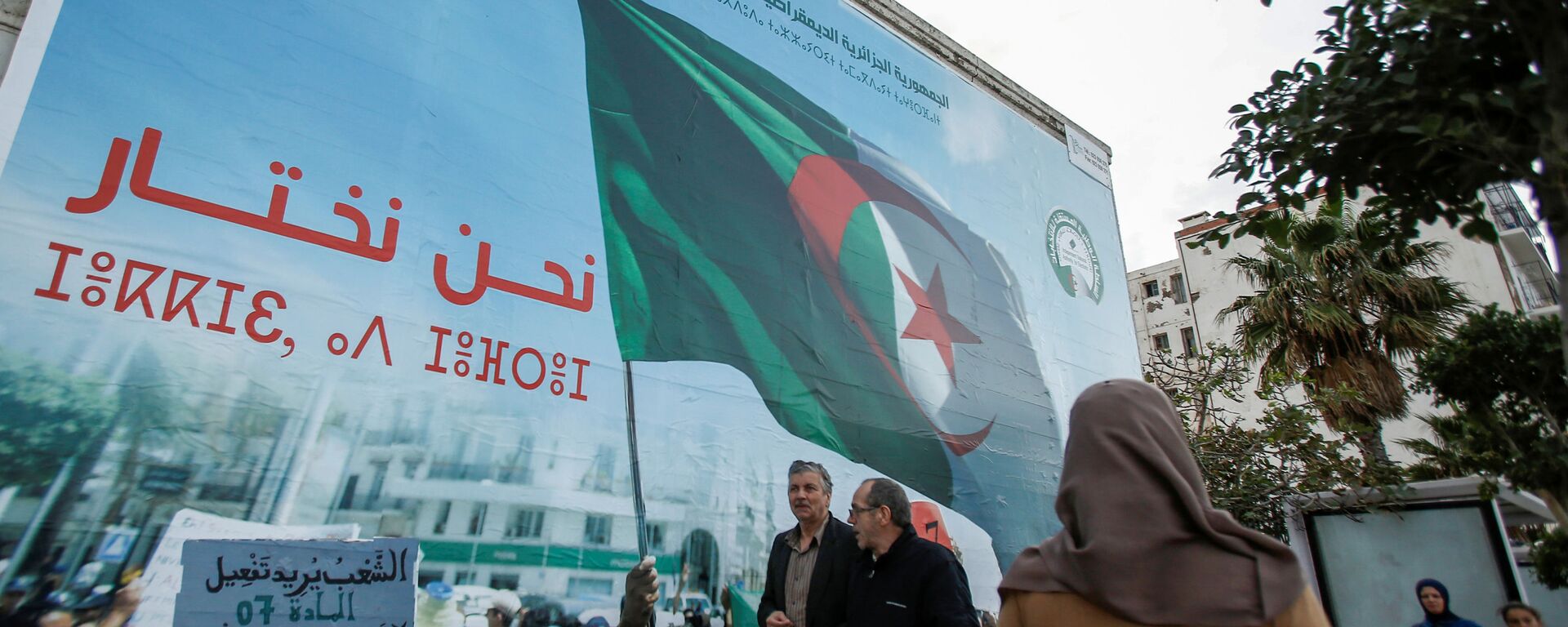 أشخاص يمشون بجوار ملصق حملة للانتخابات الرئاسية في الجزائر العاصمة - سبوتنيك عربي, 1920, 22.12.2021