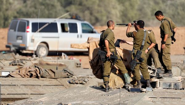 جنود إسرائيليون يفحصون سلاحهم وهم يقفون فوق ناقلة جنود مدرعة في منطقة تجمع بالقرب من الحدود مع غزة في جنوب إسرائيل - سبوتنيك عربي