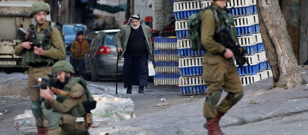 رجل فلسطيني يمشي بينما يطلق جندي إسرائيلي سلاحه خلال احتجاج على خطة الرئيس الأمريكي دونالد ترامب للسلام في الشرق الأوسط في الخليل في الضفة الغربية التي تحتلها إسرائيل - سبوتنيك عربي
