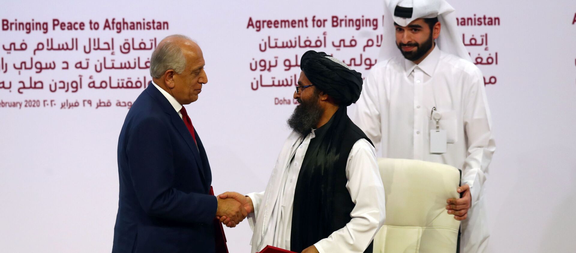 الملا عبد الغني برادار رئيس وفد طالبان وزلماي خليل زاد المبعوث الأمريكي للسلام في أفغانستان يتصافحان بعد توقيع اتفاق في حفل بين أعضاء من حركة طالبان في أفغانستان والولايات المتحدة في الدوحة - سبوتنيك عربي, 1920, 15.09.2021