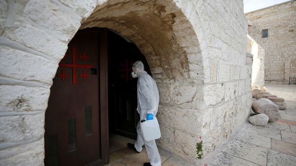 عامل يرتدي بدلة واقية يصل لتطهير كنيسة المهد كإجراء وقائي ضد فيروس كورونا في بيت لحم في الضفة الغربية التي تحتلها إسرائيل - سبوتنيك عربي